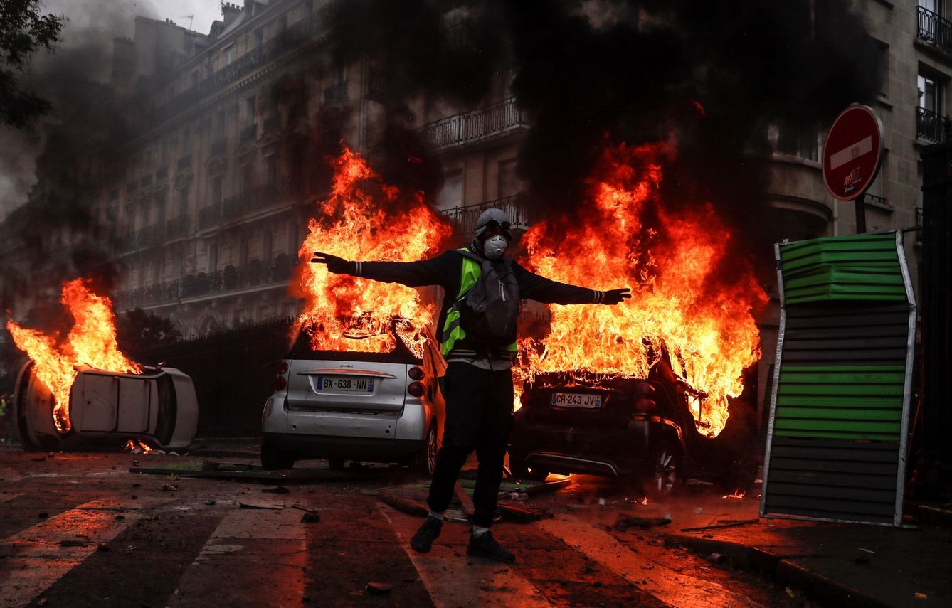 Un manifestante con un chaleco amarillo protesta por los precios del carburante junto a varios coches en llamas, en París. (EFE)