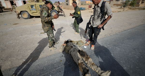 Foto: Miembros de una milicia chií observan el cadáver de un militante del ISIS tras la liberación de la ciudad de Al Qaim, en noviembre de 2017. (Reuters)