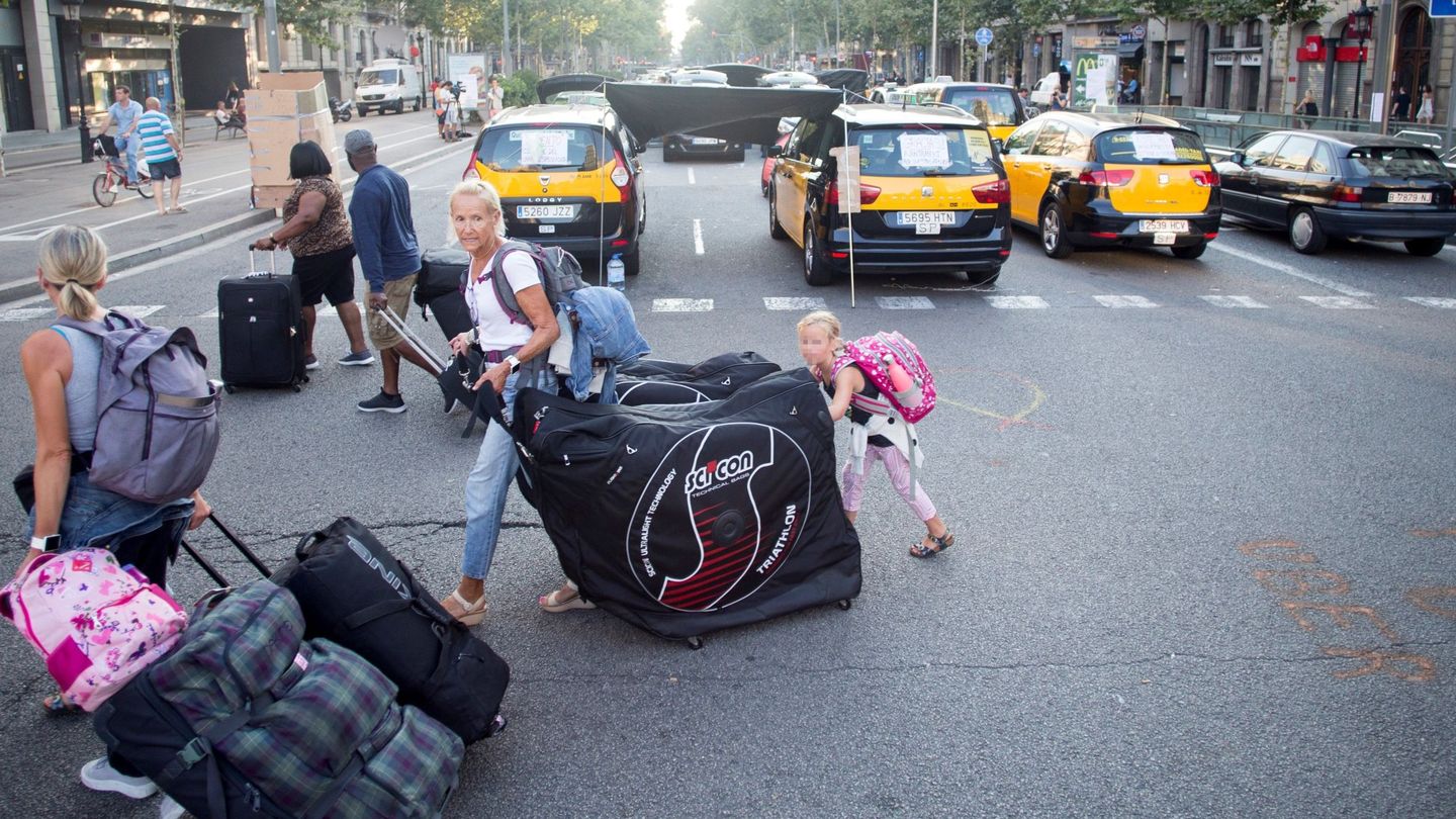 Unos turistas llevan sus maletas mientras los taxistas de Barcelona mantienen las concentraciones en el centro de la ciudad. (EFE/Quique García)