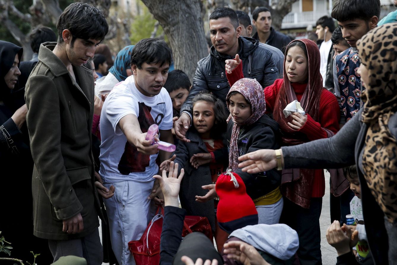 Un voluntario reparte comida a un grupo de afganos en la Plaza Victoria, Atenas (Reuters).