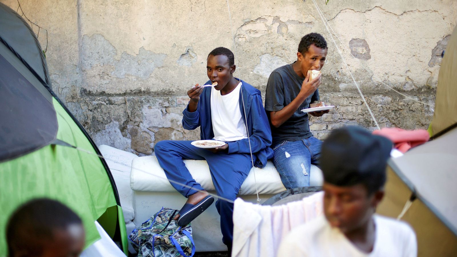 Foto: Un grupo de inmigrantes come alimentos proporcionados por voluntarios en un campamento improvisado en el centro de Roma, en agosto de 2016. (Reuters)