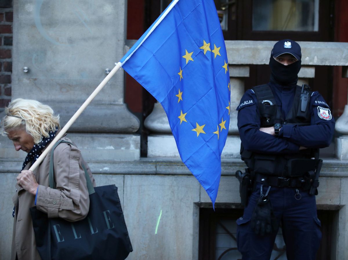 Foto: Una mujer con una bandera de la UE camina junto a un agente en una protesta. (Jakub Wlodek. Agencja Gazeta/Reuters)