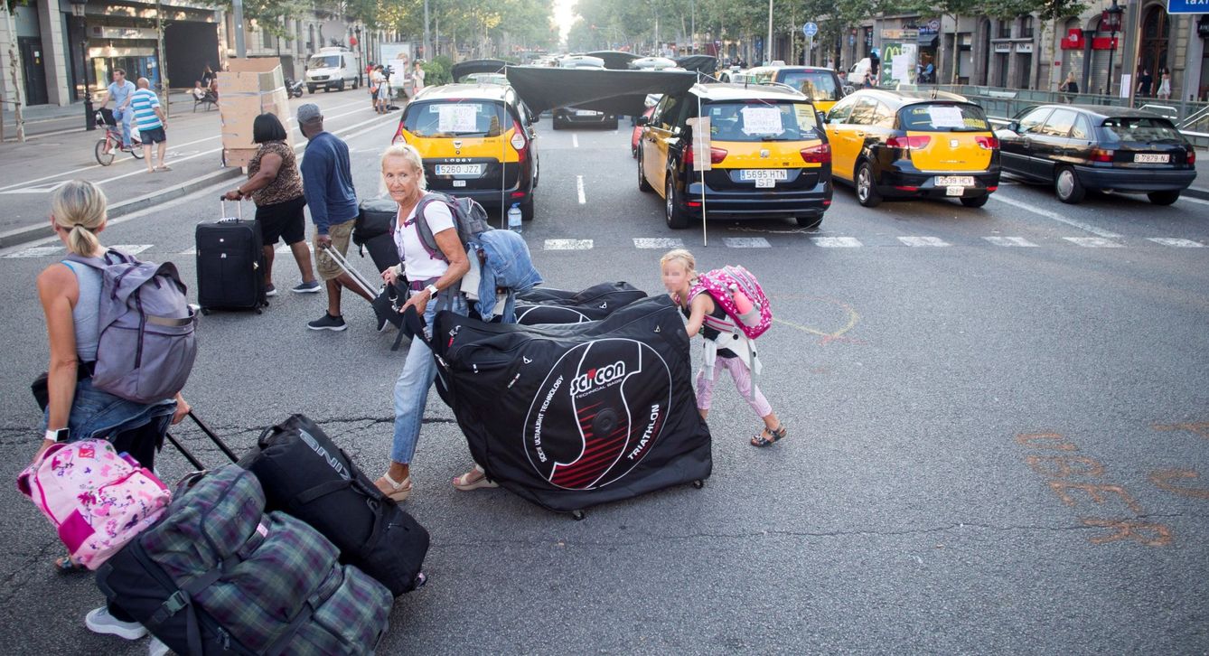 Unos turistas llevan sus maletas mientras los taxistas de Barcelona mantienen las concentraciones en el centro de la ciudad. (EFE/Quique García)