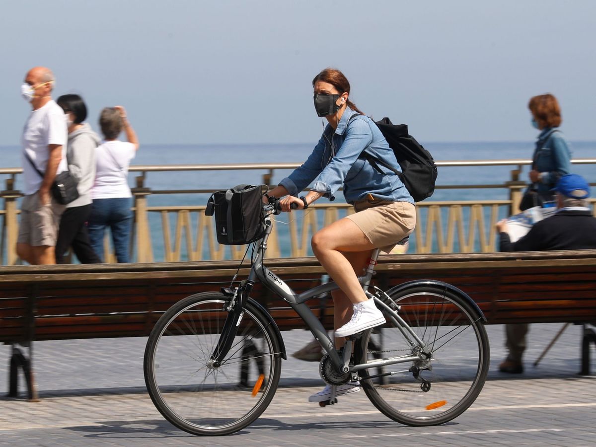 Foto: Una mujer pasea en bicicleta cubierta con una mascarilla por San Sebastián. (EFE)