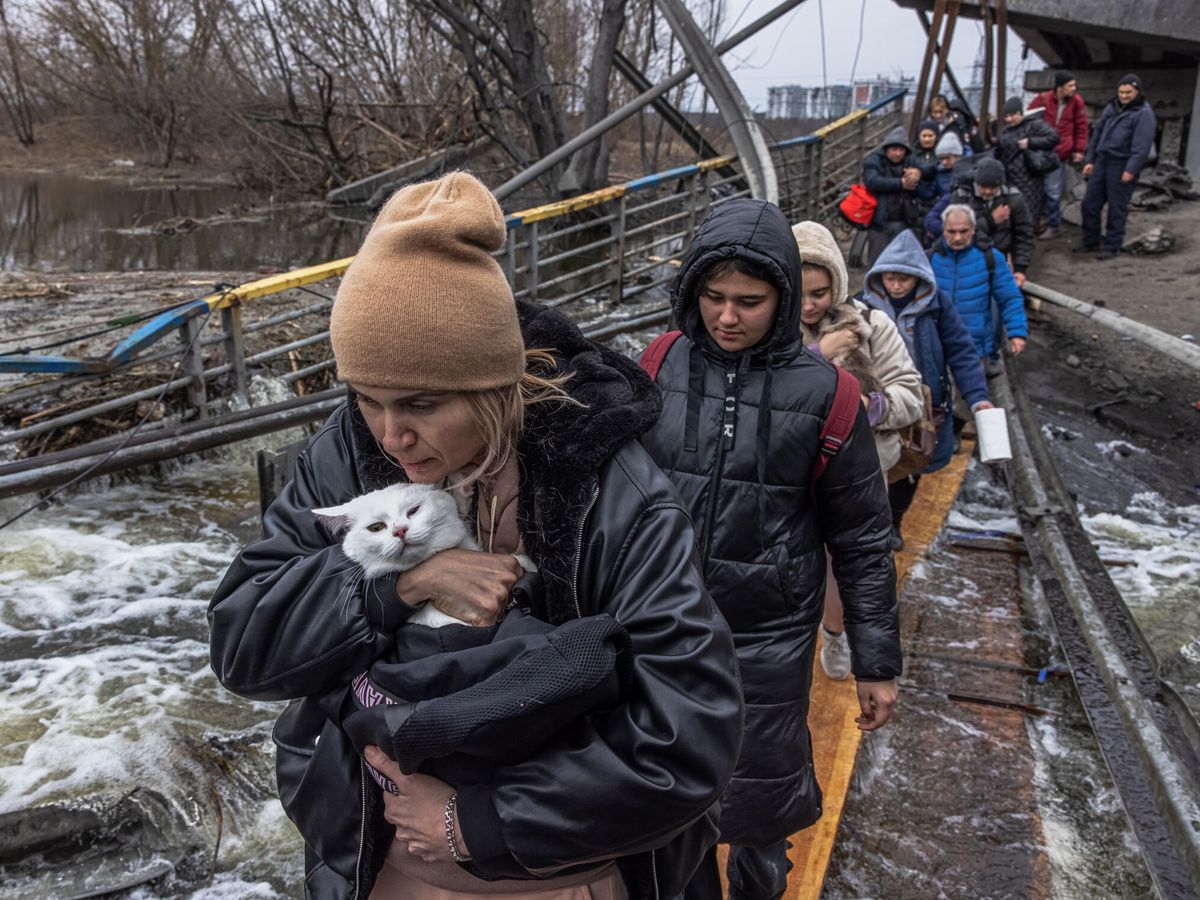 Foto: Una mujer con su gato cruza un puente destruido mientras los residentes huyen desde el frente de la ciudad de Irpín. (EFE/Roman Pilipey)