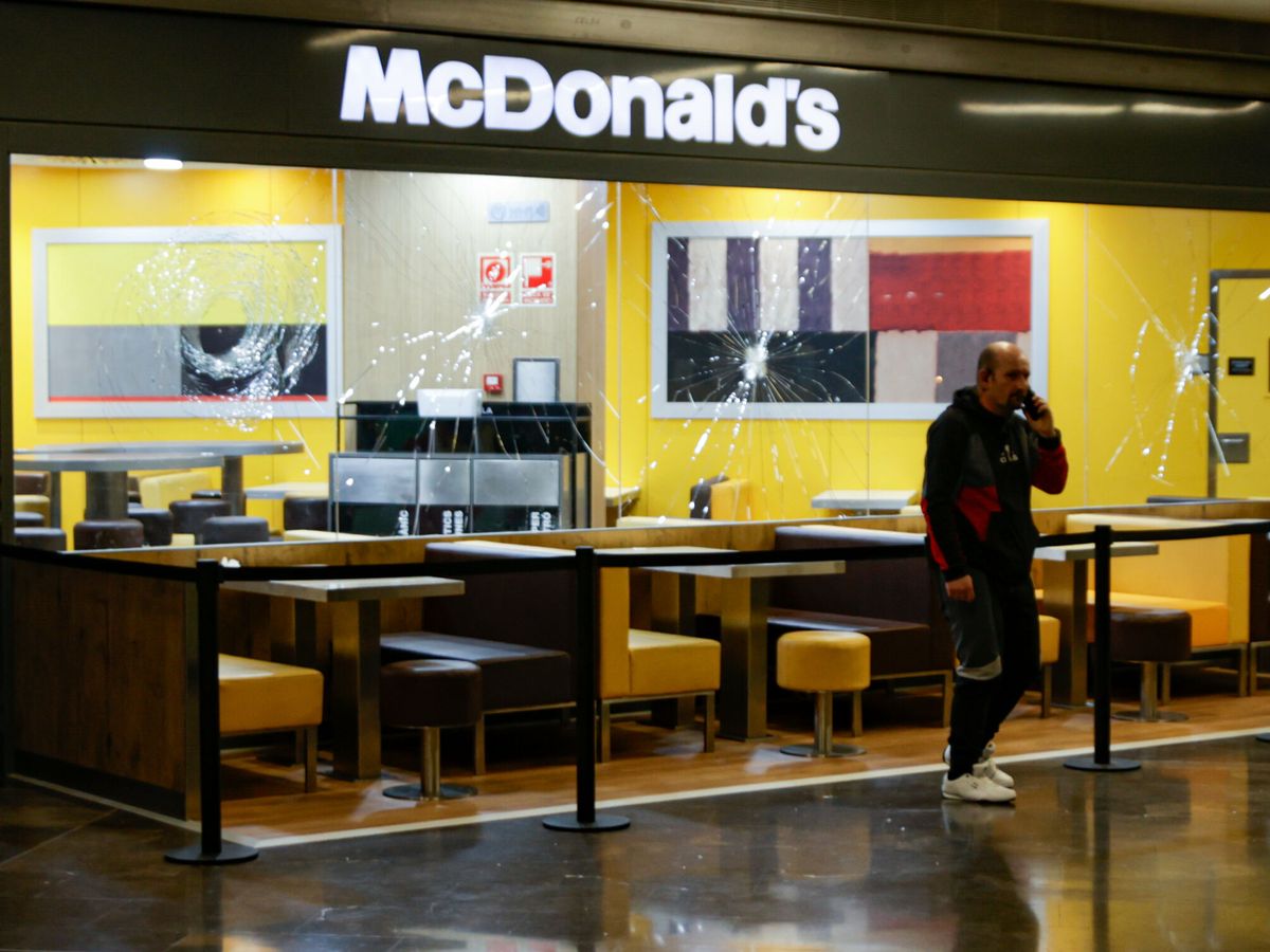 Foto: Una persona pasa delante del escaparate del McDonald's con los cristales rotos en el centro comercial Màgic Badalona. (Europa Press/Kike Rincón)