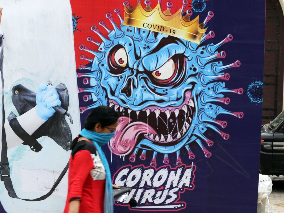 Foto: Una mujer, que se protege la boca y la nariz con una bufanda, pasa delante de un mural dedicado al coronavirus en India. (Reuters)