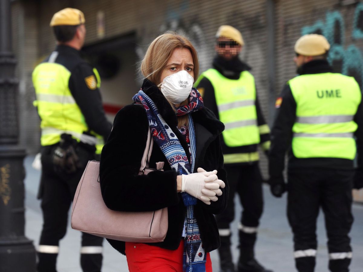 Foto: Una mujer camina con una mascarilla junto a miembros de la UME en la calle Carretas en Madrid. (EFE)