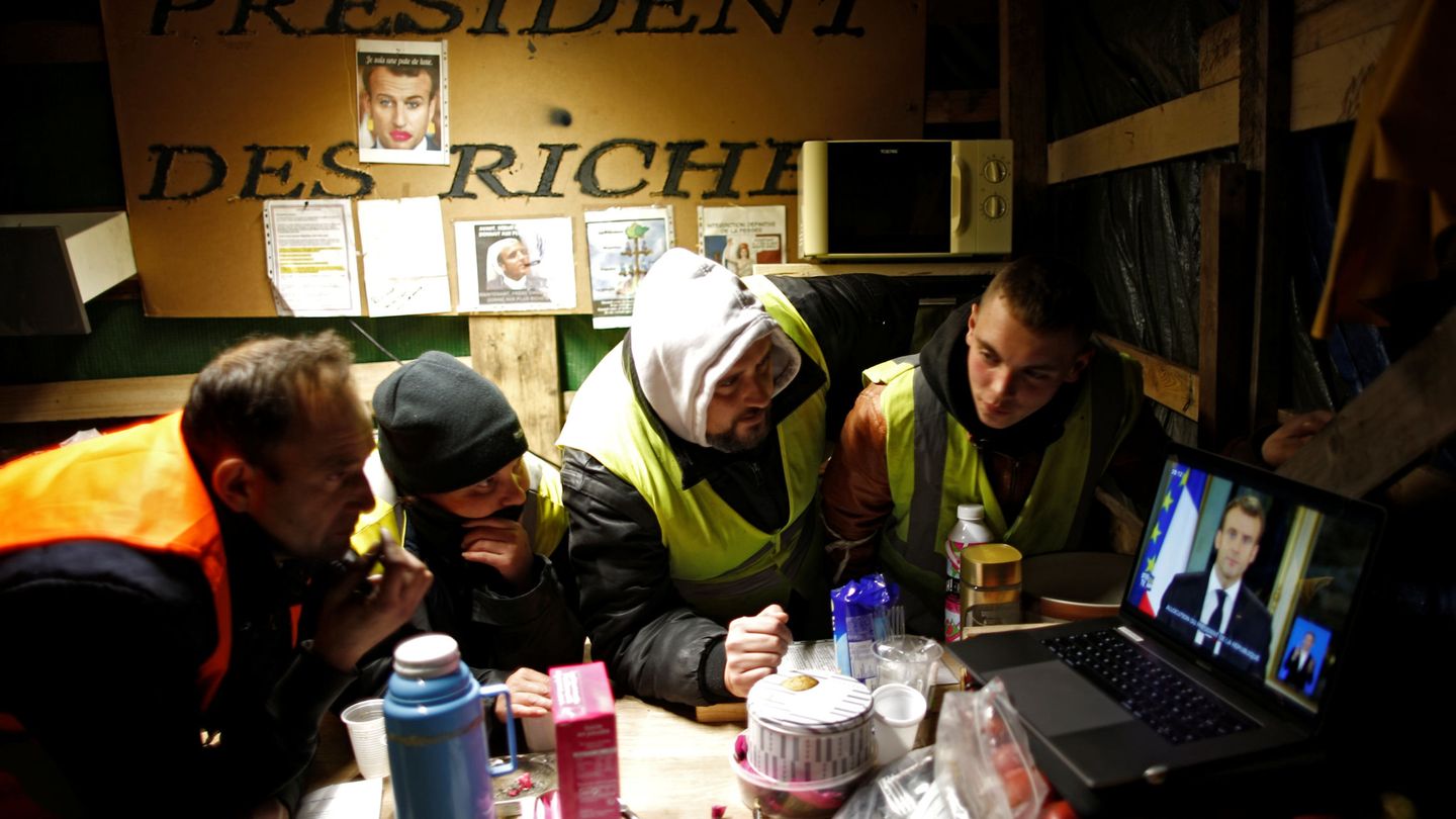 Un grupo de chalecos amarillos mira el discurso de Macron desde su campamento en Bouguenais. (Reuters)