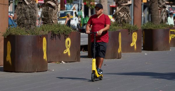 Foto: Un joven circula con su patinete ante unos lazos amarillos en el barrio de Sants de Barcelona. (EFE)