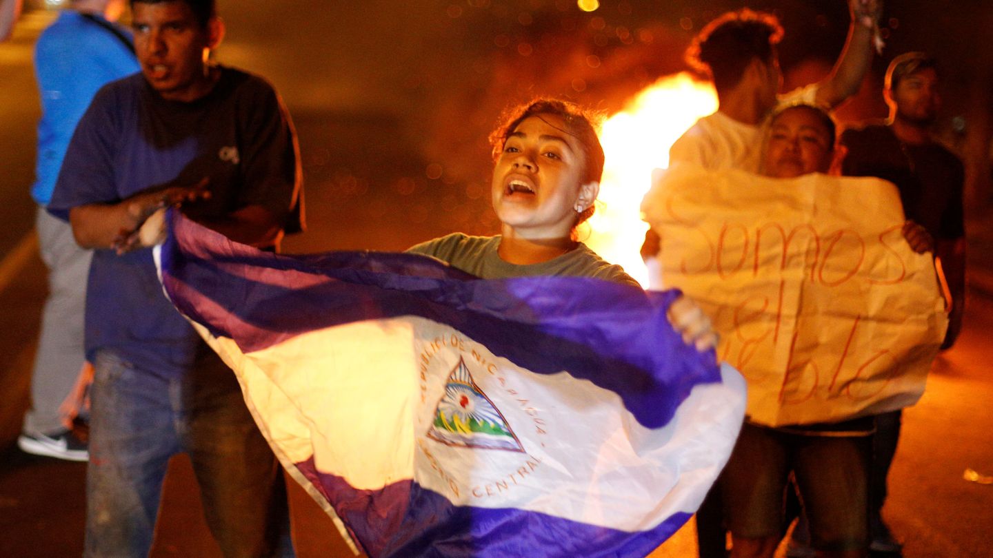 Una manifestante agita una bandera nicaragüense delante de una barricada en llamas. (Reuters)