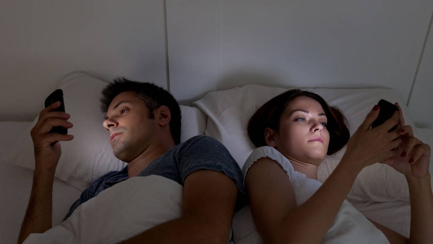 Una pareja consultando el móvil en la cama