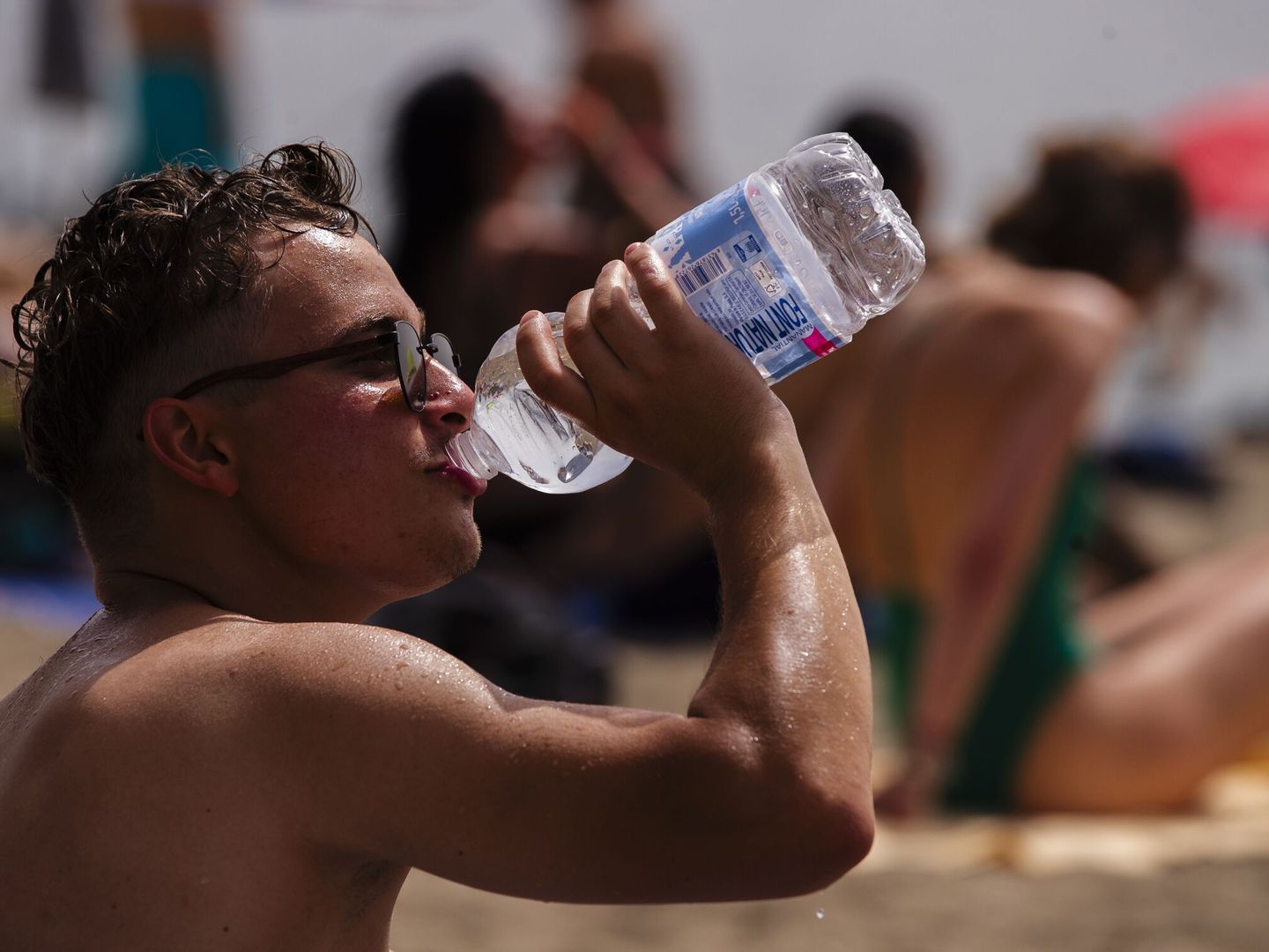Un hombre bebe agua en la playa de la Malagueta durante la ola de calor. (EFE/Jorge Zapata)