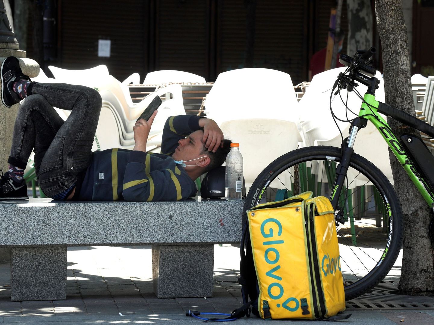 Un repartidor de comida a domicilio descansa en un banco de la plaza Santa Ana en Madrid. (EFE)