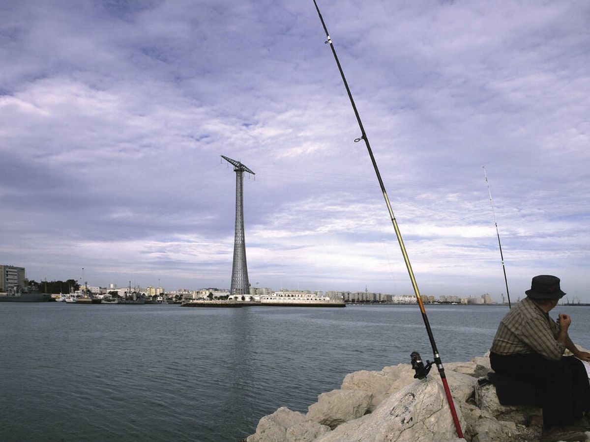 Foto: Un pescador sentado en el espigón, con el barrio de Puntales al fondo. (Ayuntamiento de Cádiz)