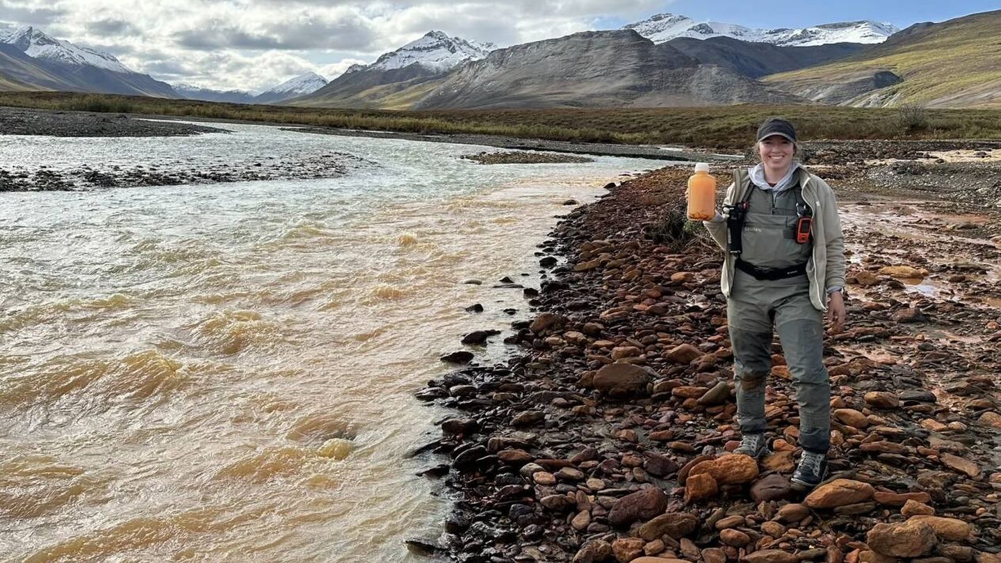 Taylor Evinger sostiene una botella de agua de color naranja tomada del río Igning en el Parque Nacional y Reserva Gates of the Arctic en Alaska (Brett Poulin/UC Davis)