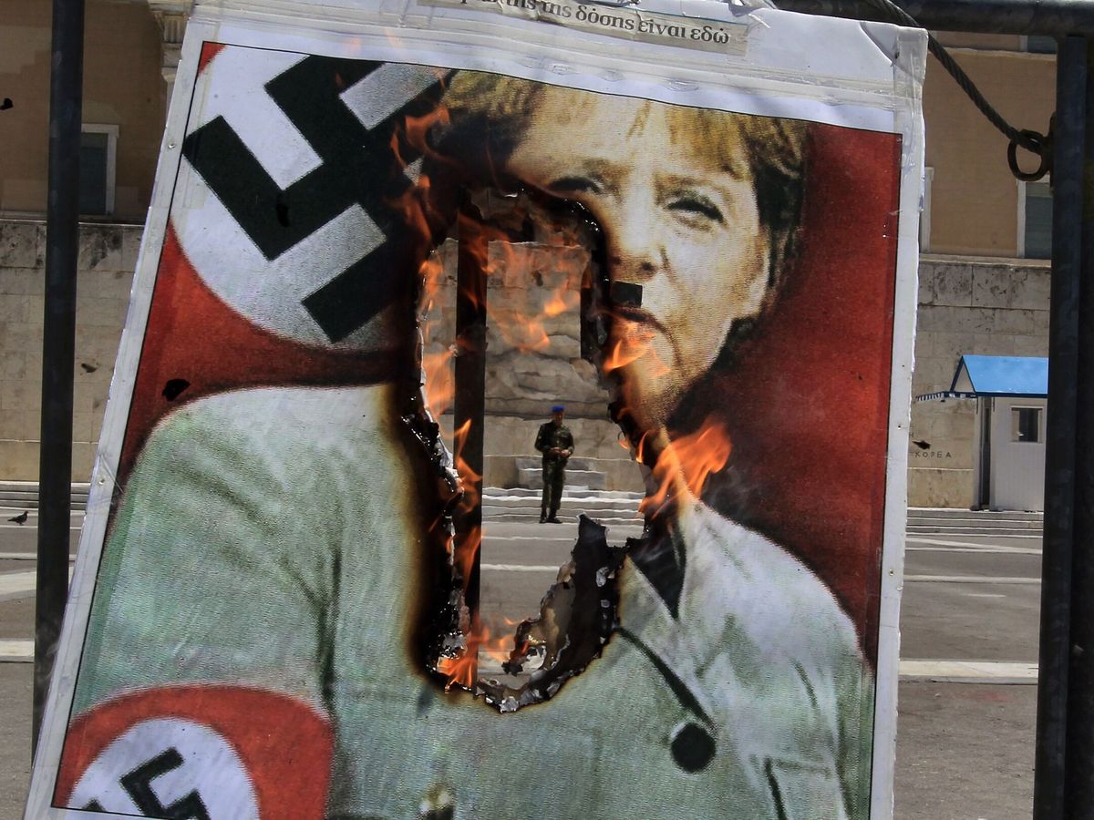 Foto: Quema de una foto de Angela Merkel con indumentaria nazi frente al Parlamento griego. (EFE/Simela Pantzartzi)