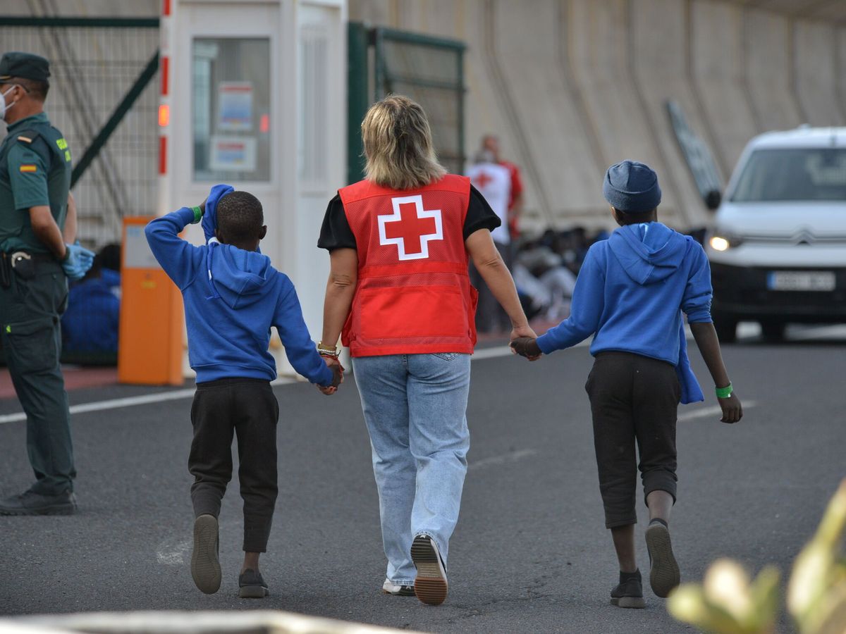 Foto: Una trabajadora de Cruz Roja escolta a dos menores inmigrantes llegados a Canarias. (EFE/Gelmert Finol)