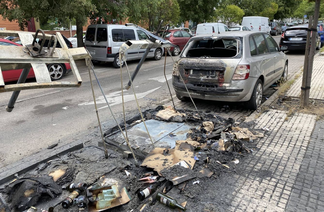 Foto: Un contenedor calcinado, junto a un coche quemado este lunes, en la calle Beasaín, en Orcasitas. (C. B.) 
