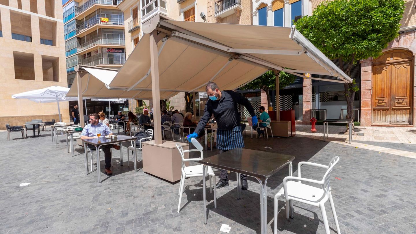 Un camarero desinfecta una mesa tras un servicio en una terraza de la Plaza del Cardenal Belluga de Murcia. (EFE)