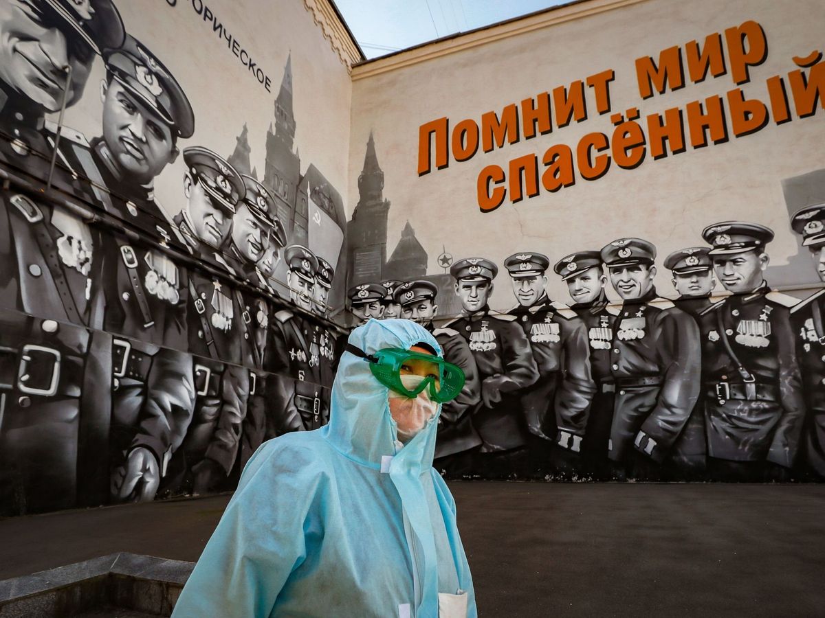 Foto: Una mujer con traje protector, junto a un mural gigante dedicado a la victoria rusa en la Segunda Guerra Mundial. (EFE)