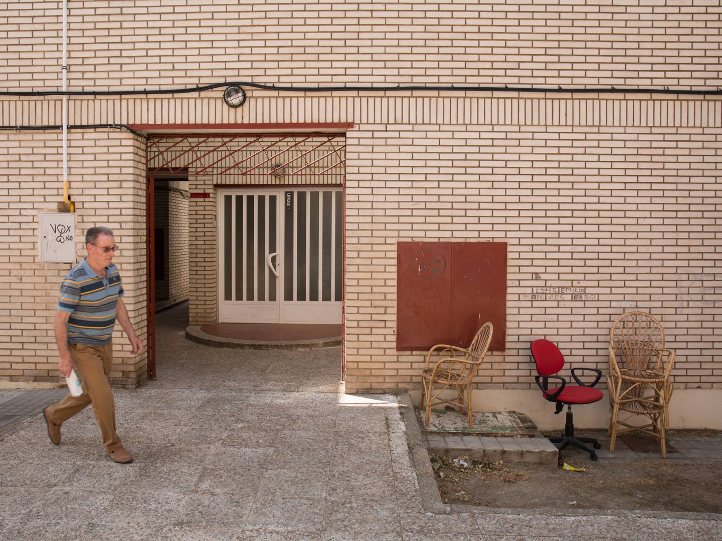 Un vecino pasa frente a la entrada de un bloque de viviendas en La Granja, Ciudad Real.