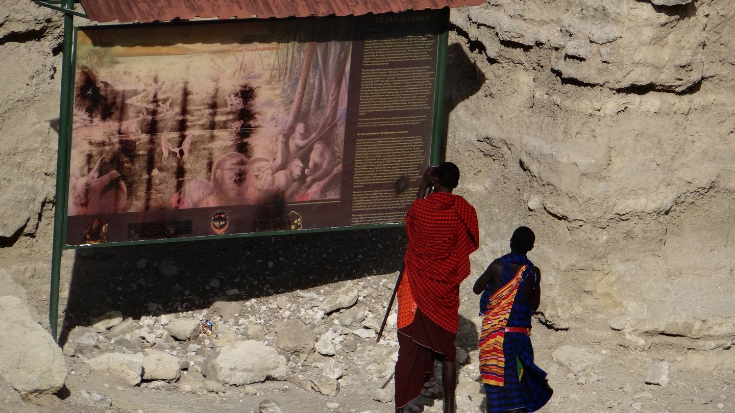 Dos masáis observan en Olduvai un panel de los yacimientos puesto por los españoles. (Foto: Antonio Pérez Henares)
