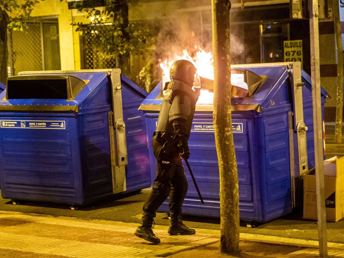 Foto: Un agente de la policía junto al contenedor de papel que arde durante los distrubios en Logroño. Foto: Efe