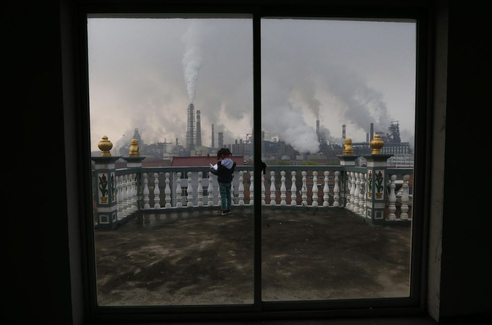 Una niña lee en el balcón mientras el humo se eleva de las fábricas en Quzhou (Reuters).