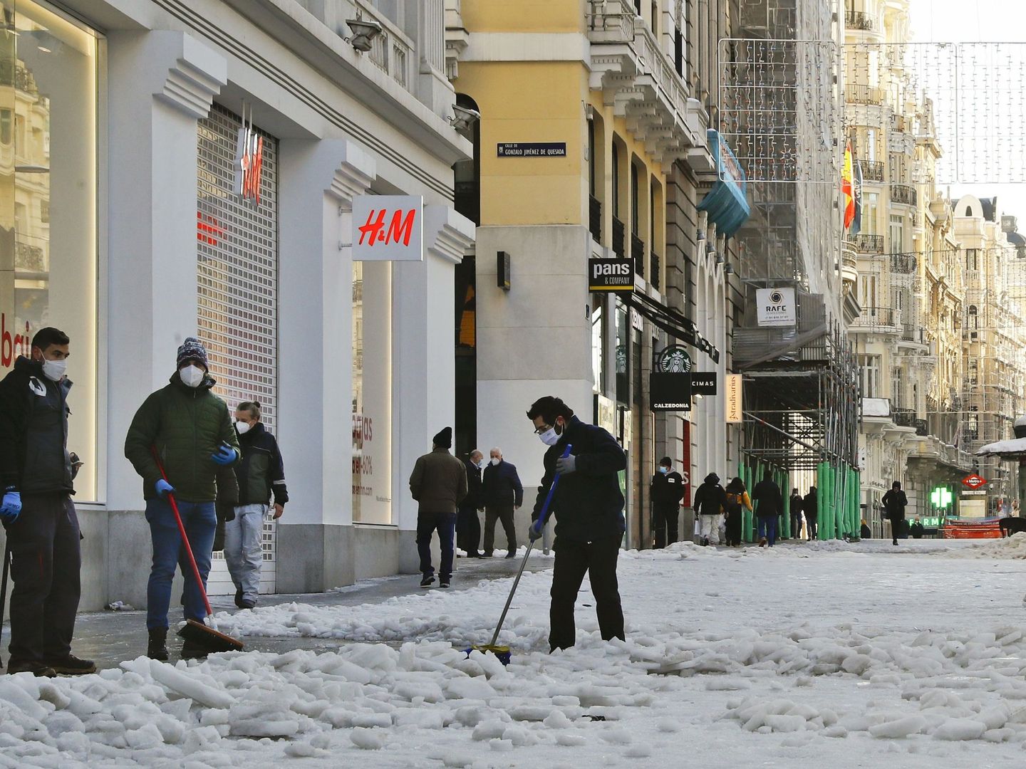 Varias personas limpian la nieve de los comercios de la Gran Vía en Madrid. (EFE)