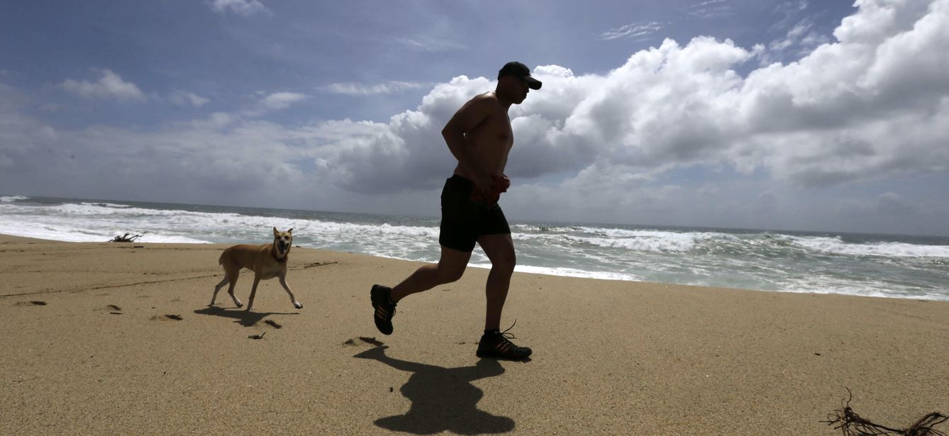 Un 'runner' corre acompañado de su perro en una playa de California (Reuters)