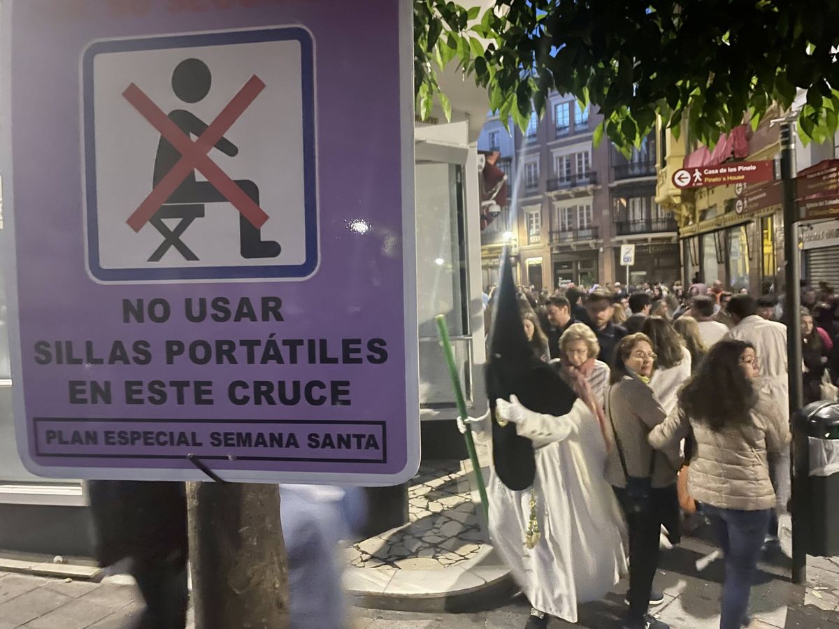 Foto: Un nazareno de la Macarena pasa junto a un cartel que prohibe el uso de sillas portátiles. Foto: José Luis Losa
