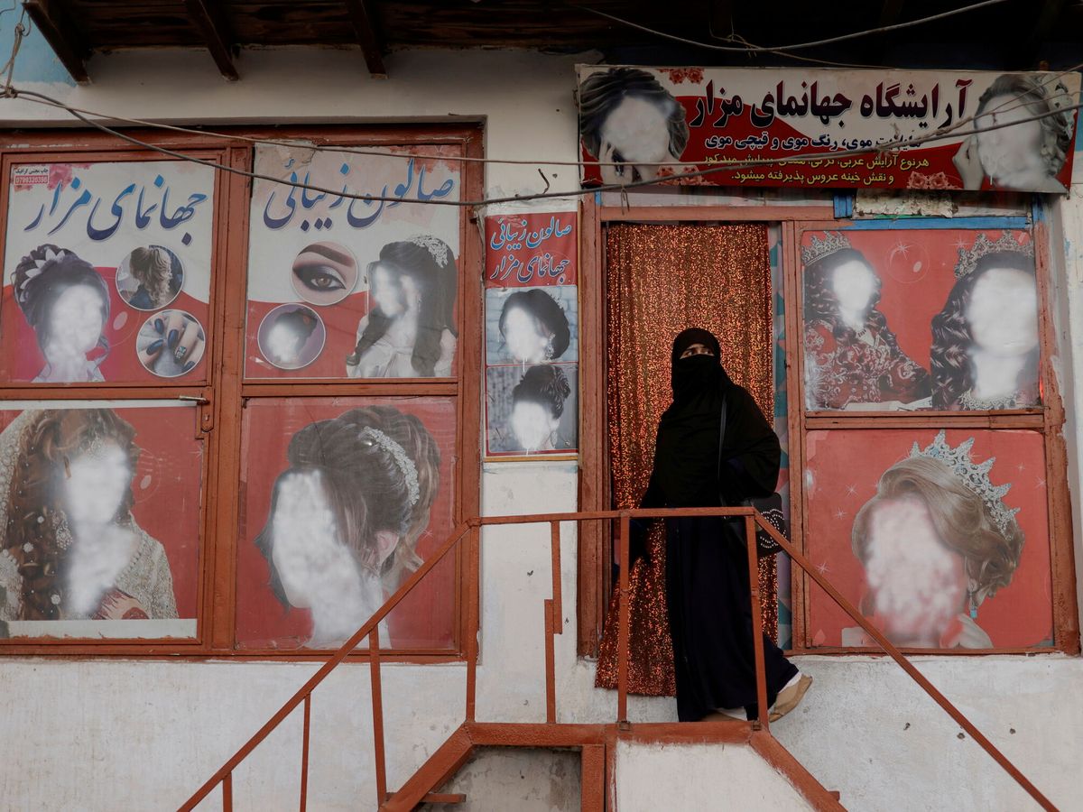 Foto: Una mujer vestida con un niqab entra en un salón de belleza donde un comerciante ha desfigurado los anuncios de mujeres en Kabul, Afganistán. (Reuters/Jorge Silva)