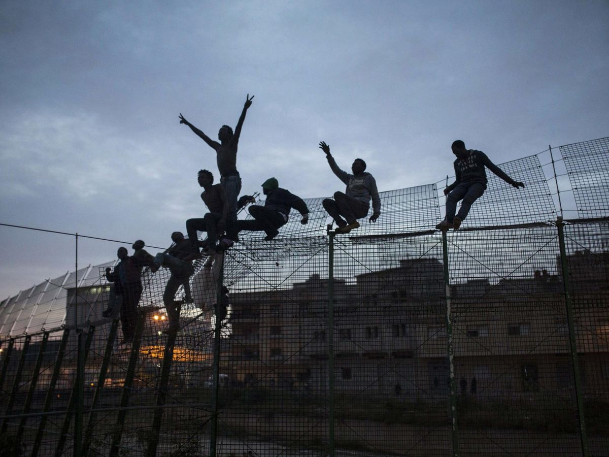 Foto: Varios inmigrantes encaramados a la valla de Melilla en un salto de 2015. (EFE)