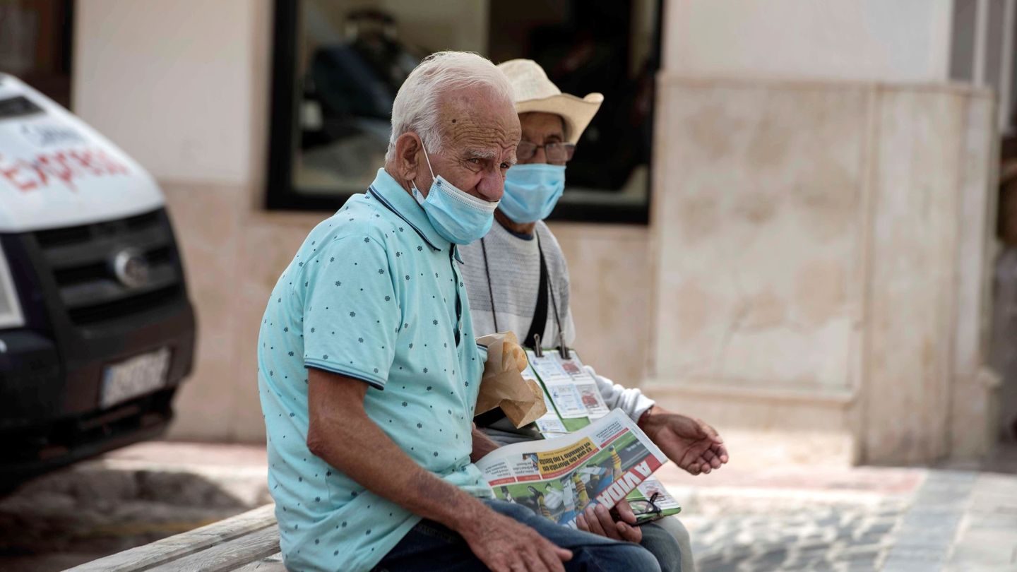Una pareja de ancianos se protege con mascarillas mientras descansan en un banco en Mahón. (EFE)