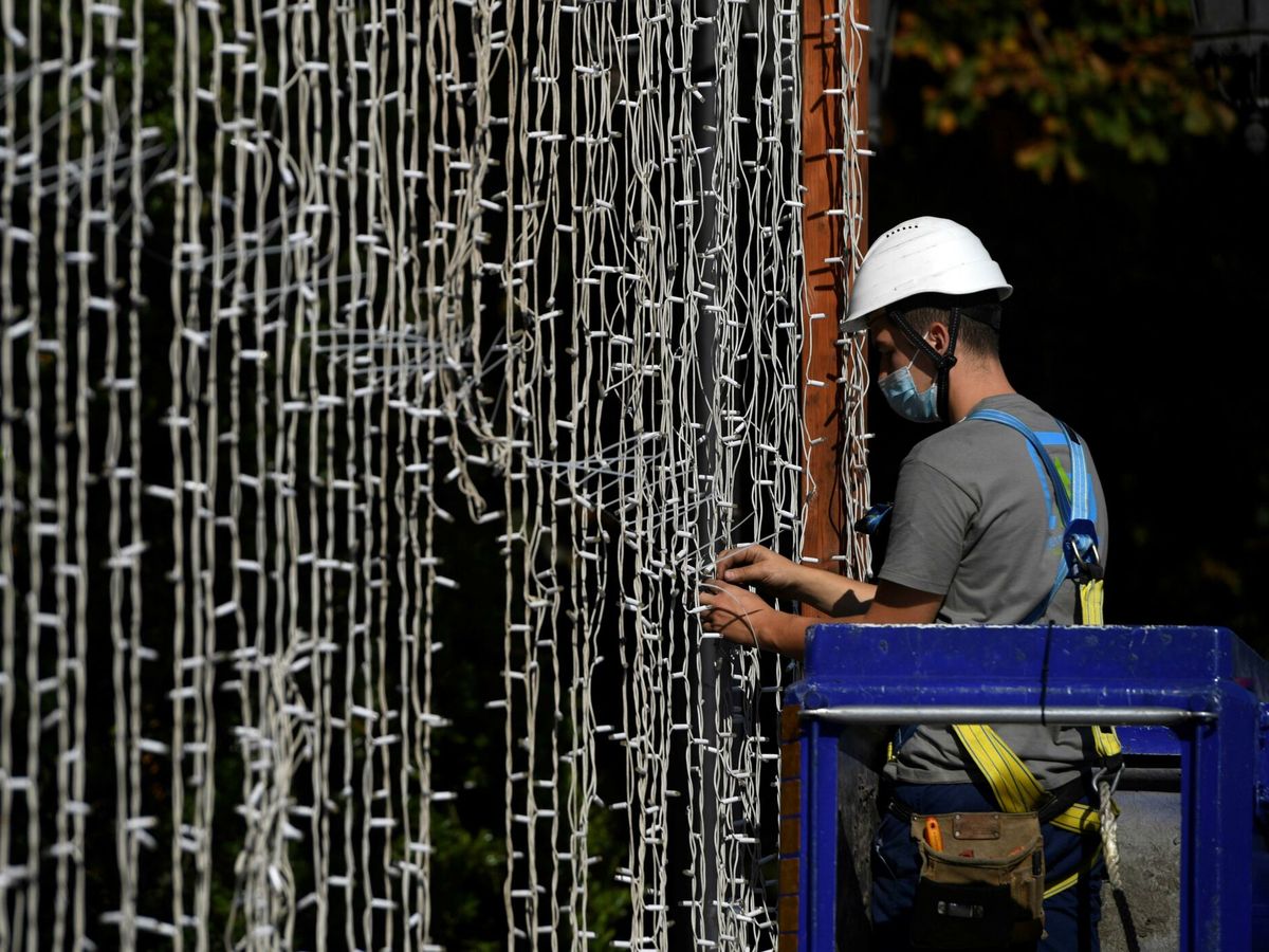 Foto: Un operario coloca una cortina de luces led en un parque de Oviedo. (EFE)
