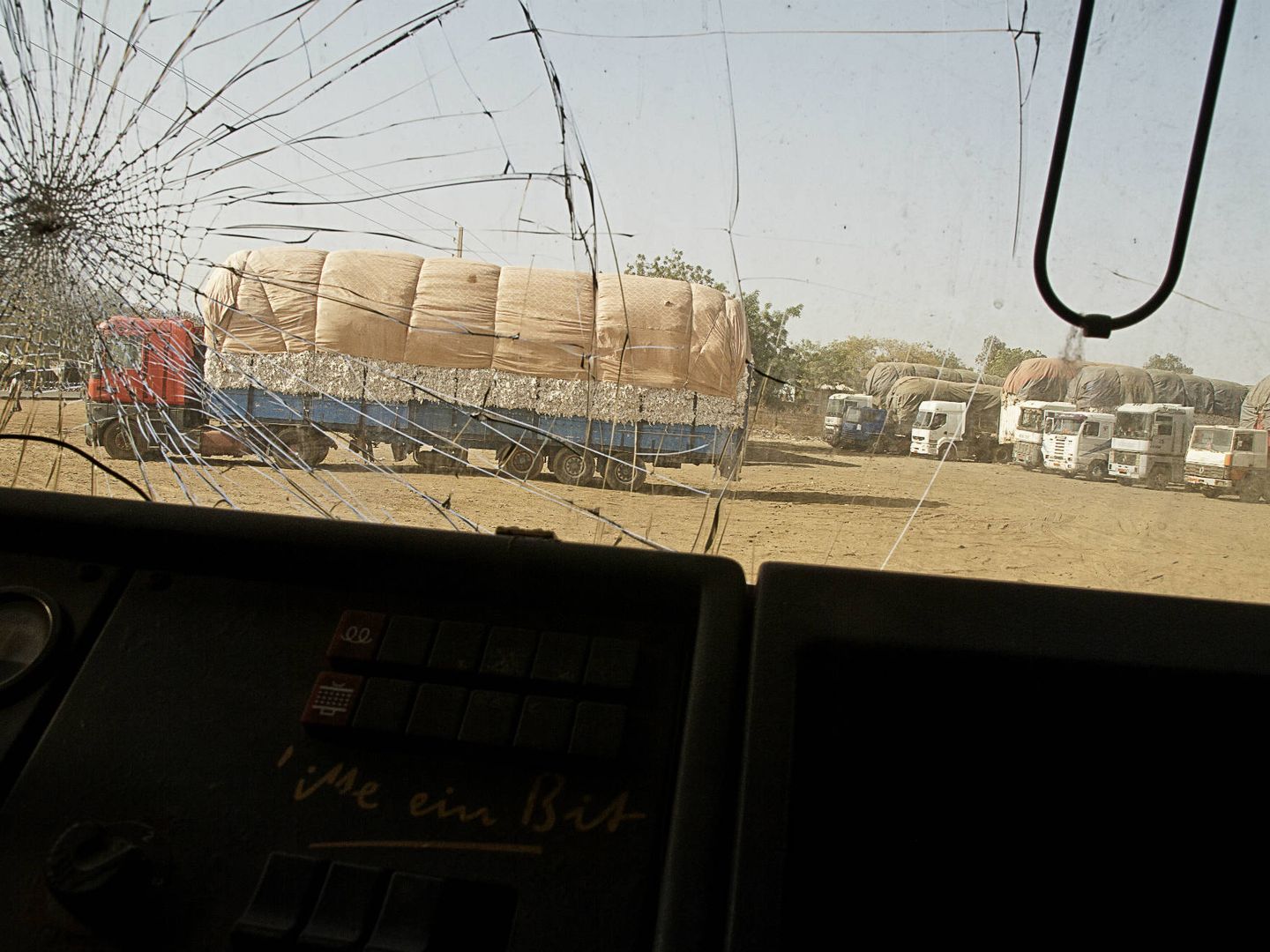 Camiones aparcados delante de la planta de procesamiento de algodón, vistos desde el parabrisas agrietado de otro vehículo (K. Gómez)