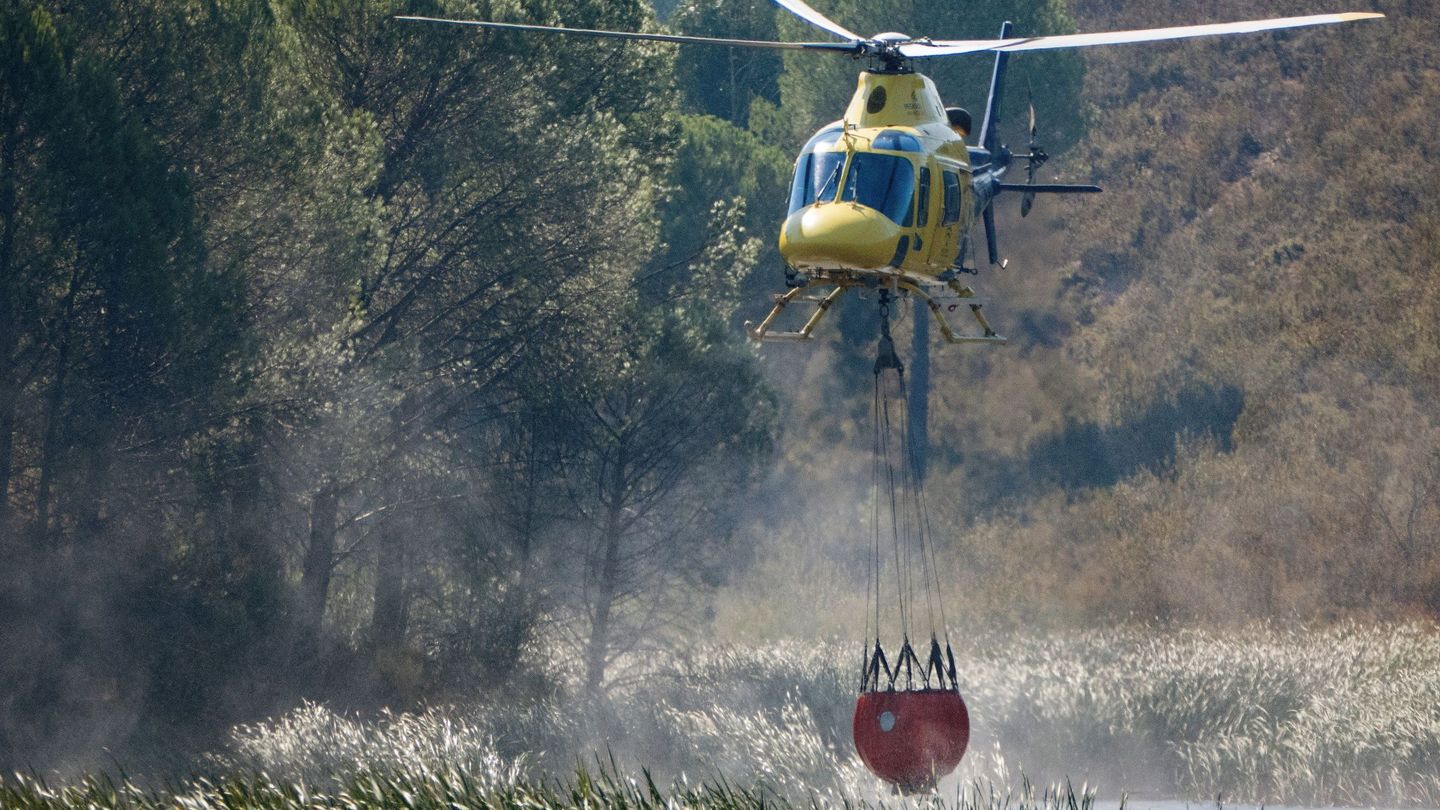Un helicoptero carga agua para sofocar el avance de las llamas y el fuerte viento en el incendio forestal de Almonaster la Real, en Huelva. (EFE)