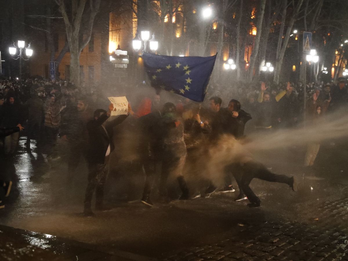 Foto: Manifestantes en Tbilisi aguantan los golpes de los cañones de agua alrededor de una bandera de la UE. (EFE)