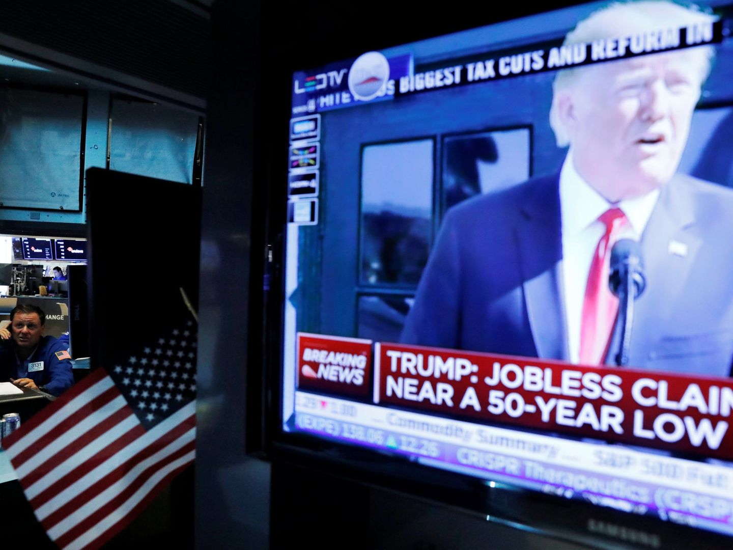 Un 'broker' habla por teléfono en la Bolsa de Nueva York mientras Donald Trump habla en la televisión, el 27 de julio de 2018. (Reuters)