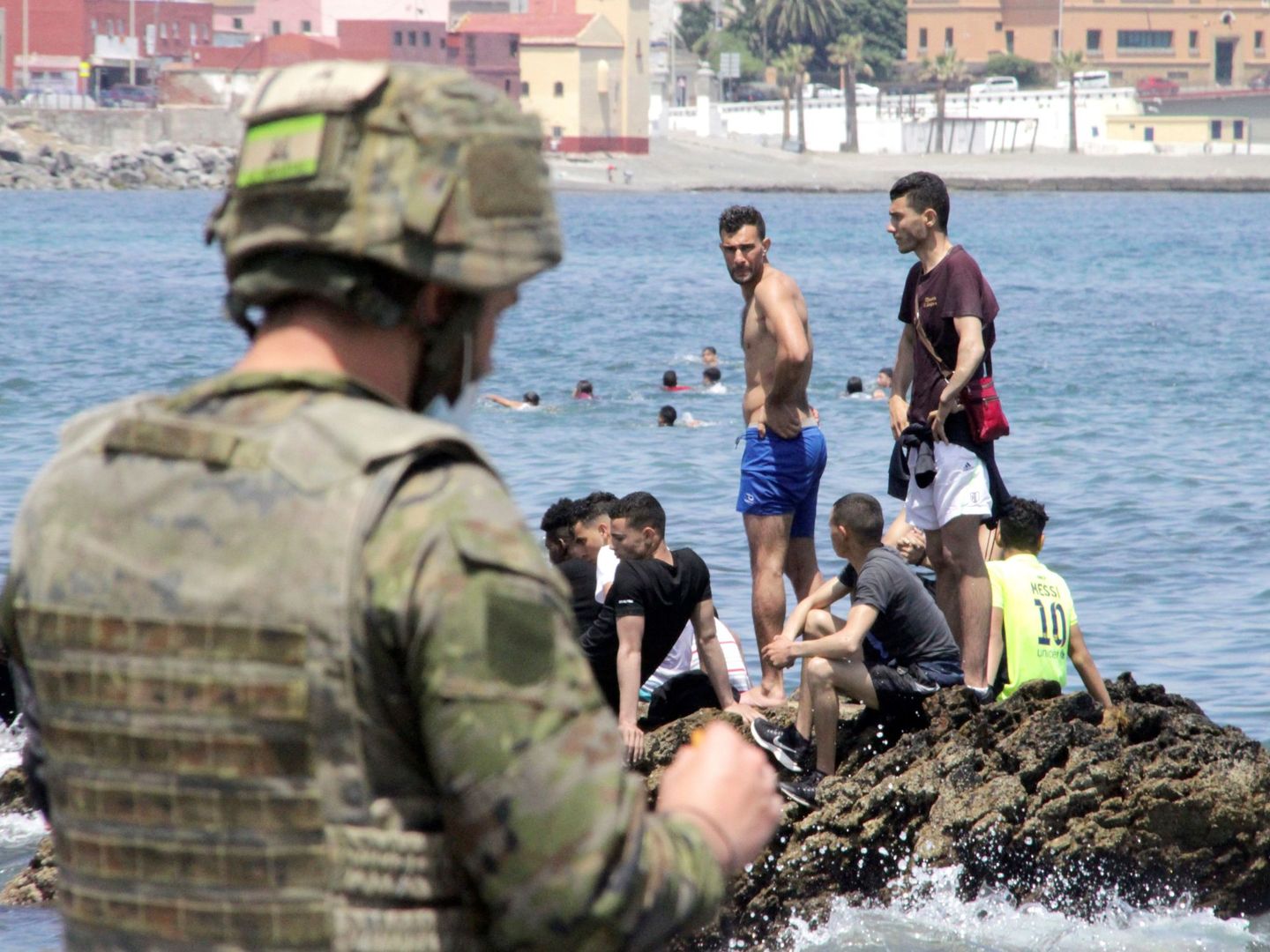Un soldado observa a varios inmigrantes en la playa fronteriza de El Tarajal, en Ceuta. (EFE)