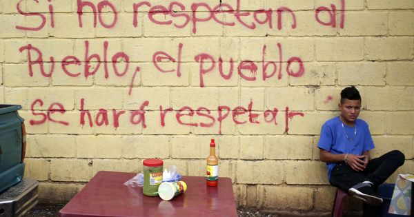 Foto: Un joven vende comida frente a un grafiti en una pared exterior de la sede del Tribunal Supremo Electoral de Tegucigalpa (Honduras). (EFE)