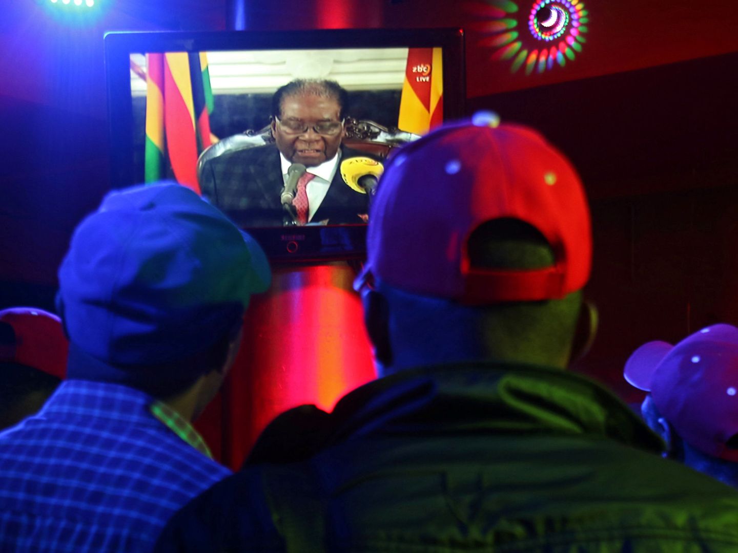 Ciudadanos de Zimbabue miran un discurso de Robert Mugabe desde su arresto domiciliario, en un bar de Harare, el 19 de noviembre de 2017. (Reuters)