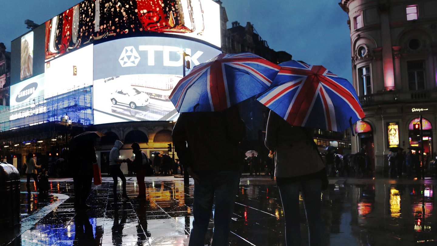 Dos personas se protegen de la lluvia con paraguas con la bandera en Piccadilly Circus (Reuters).