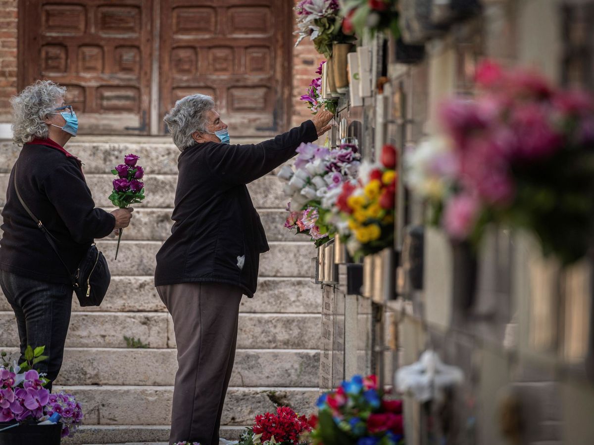 Foto: Dos mujeres colocan flores en una tumba del cementerio de Alcalá. (EFE)