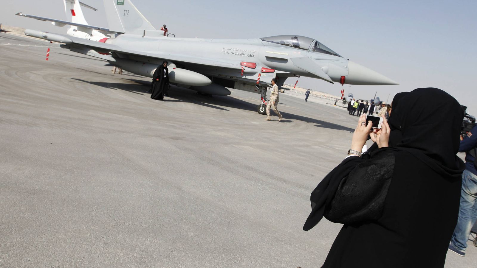 Foto: Una mujer fotografía a su amiga delante de un caza saudí durante una exhibición aérea en la base de Sakir, en Bahréin. (Reuters)