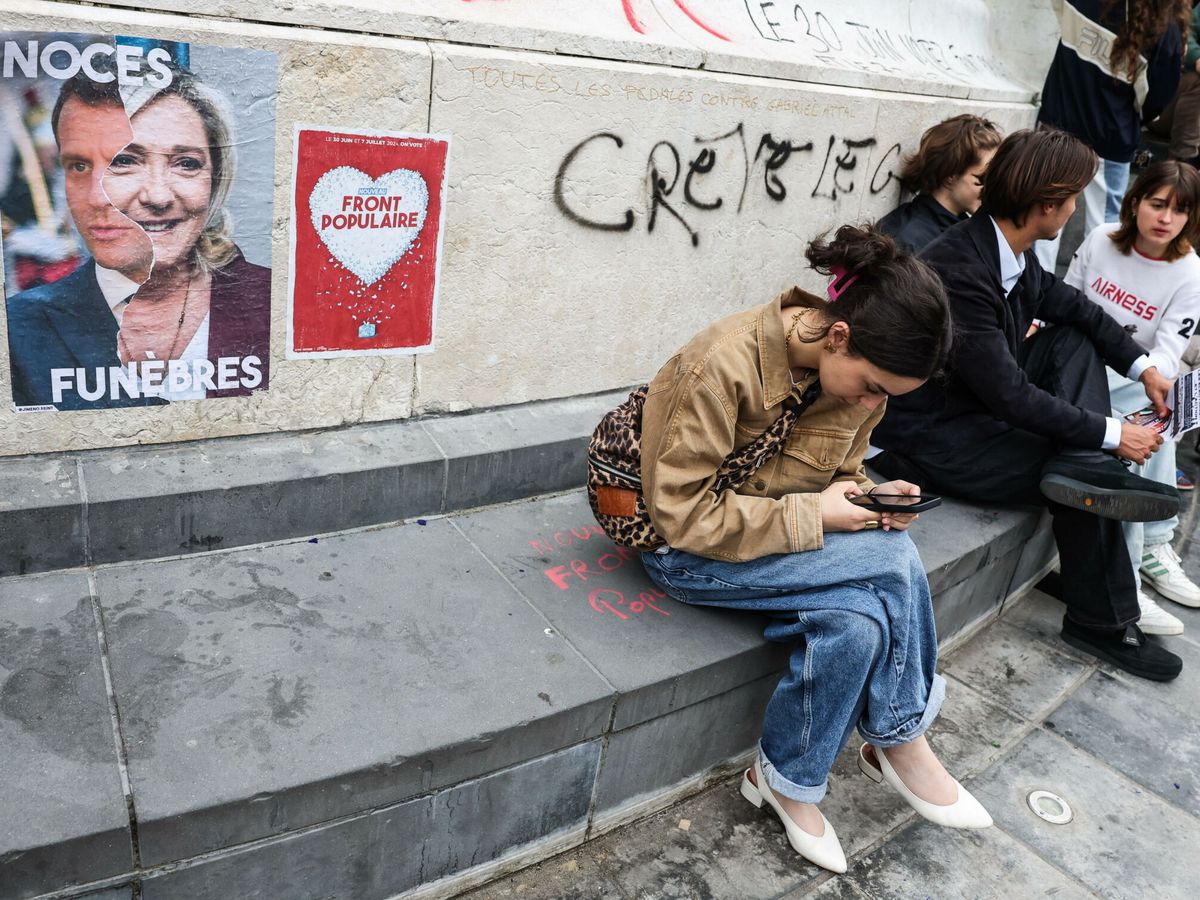 Foto: Un grupo de jóvenes se siente junto a unos carteles electorales en París. (EFE/EPA/Mohammed Babra)