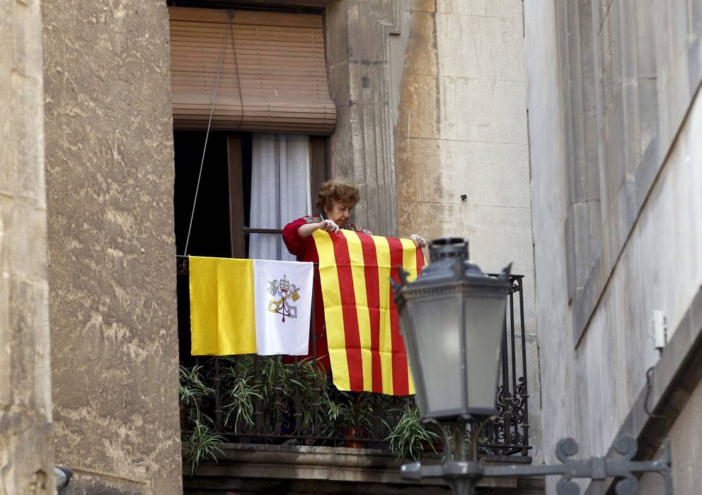 Foto: Una mujer coloca en su balcón una señera de Cataluña junto a otra del Vaticano, en 2010, durante la visita del anterior Papa, Benedicto XVI. (EFE)