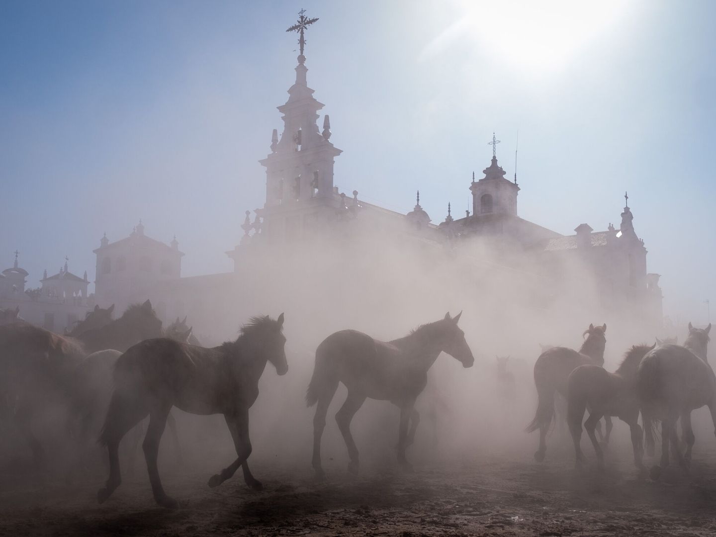 Alrededor de 1.500 cabezas de equinos en estado semisalvaje pasan delante de la ermita de El Rocío. (EFE/Julián Pérez)