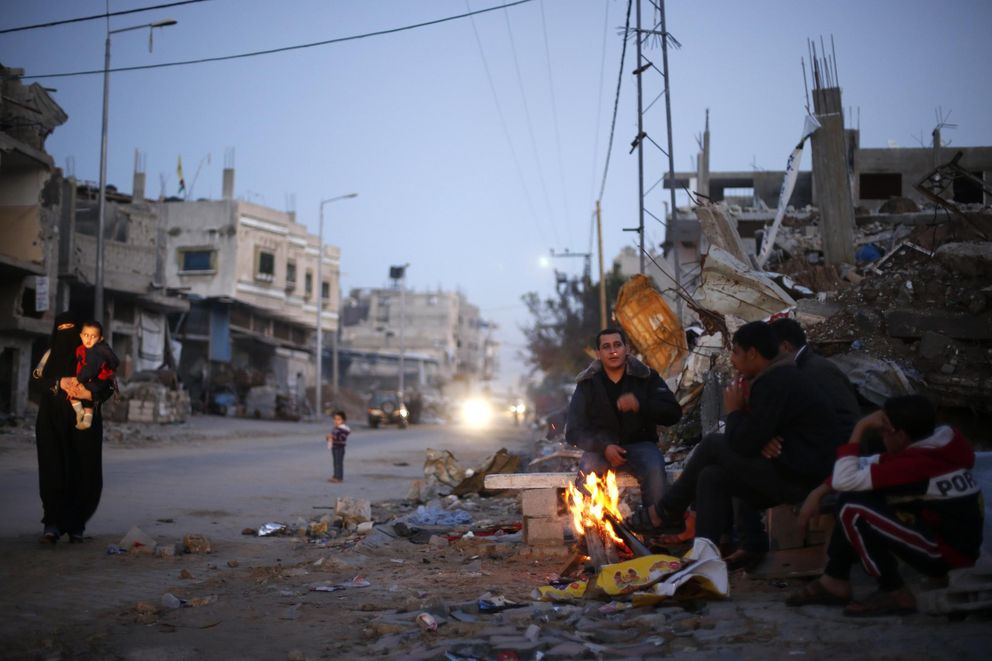 Palestinos se calientan con un fuego ante los restos de sus casas destruidas por ataques aéreos en Gaza (Reuters).